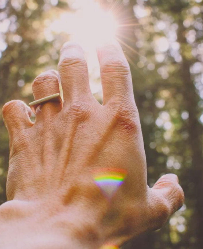 Hand reaching to sunlight with prism of chakra colors